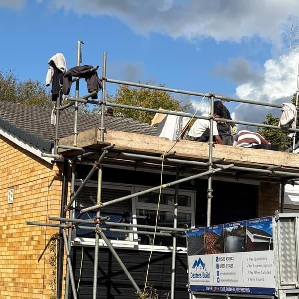 Scaffolding up at the front of the bungalow, with the new grey tiles on the roof and the Dexters Build trailer on the drive